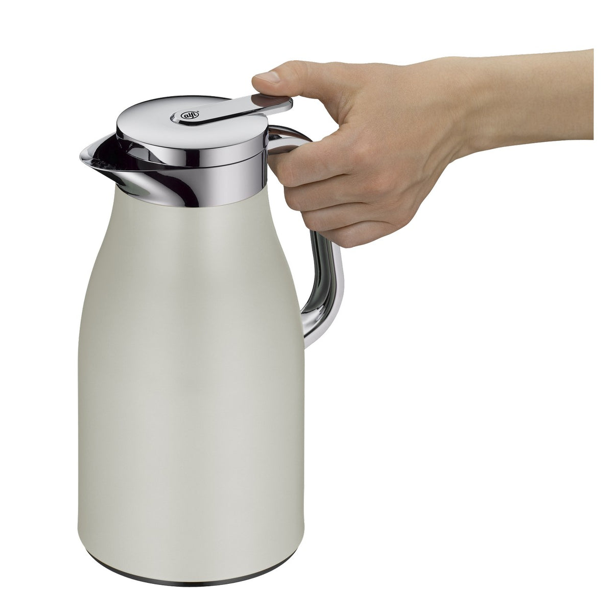 Auf dem Bild steht eine elegante, weiße Thermoskanne mit silbernem Deckel und Griff auf einem Holztisch. Im Hintergrund sind verschwommen Bürotürme und grüne Bäume zu sehen. Die Szene ist ruhig und modern gehalten.