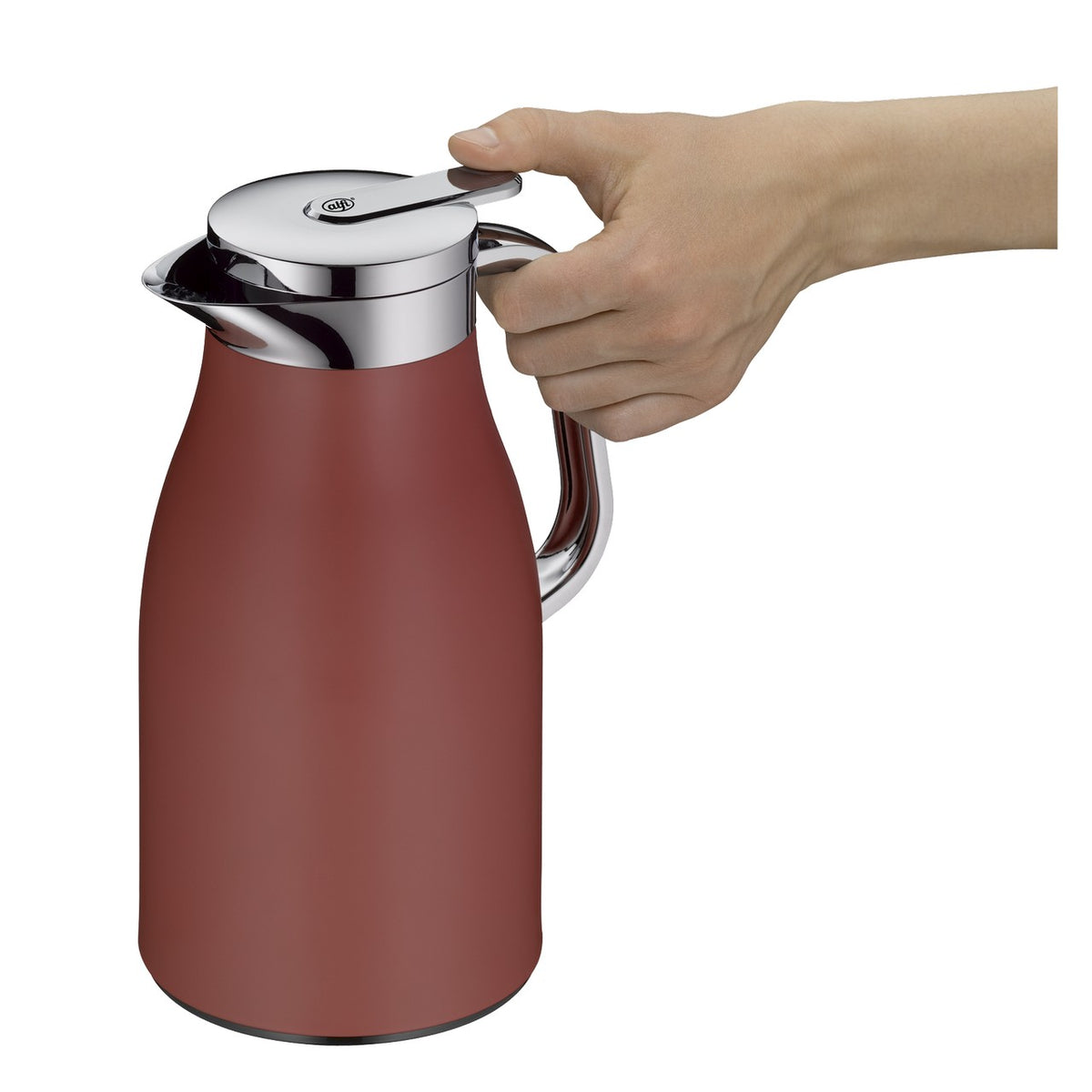 Auf einem Tisch steht eine rote Thermoskanne neben einem Teller mit aufgeschnittenen Grapefruits. Im Hintergrund sitzt eine Person entspannt auf einem Stuhl und hält eine Tasse in den Händen. Die Szene wirkt gemütlich und einladend.