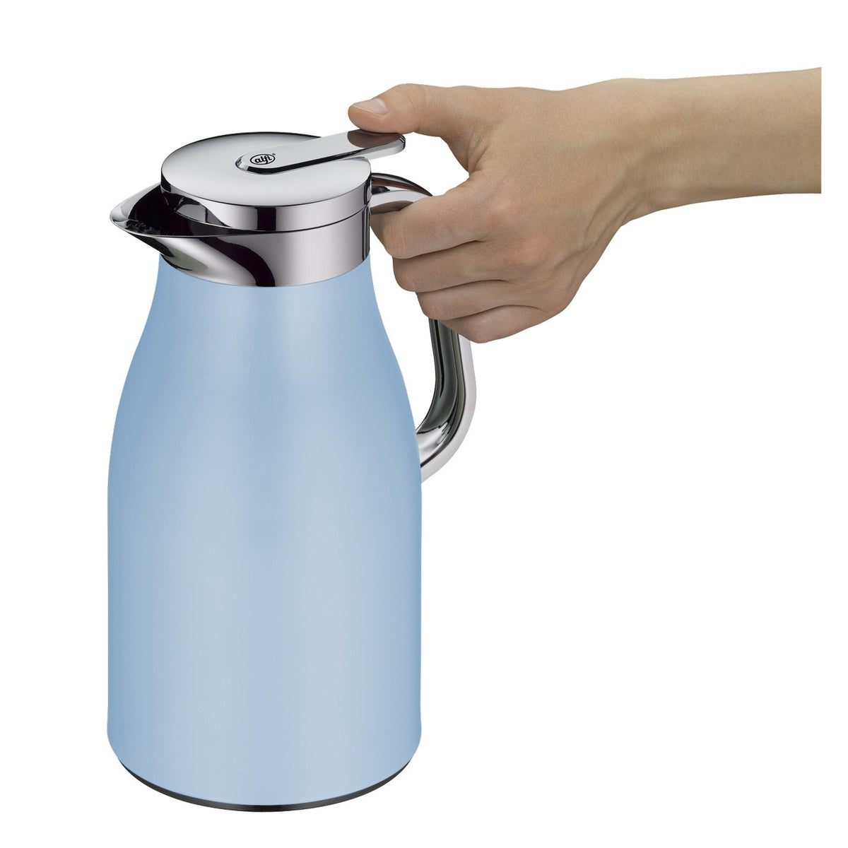 Auf einem Küchentresen steht eine hellblaue Thermoskanne neben Gewürzmühlen, einer Tasse und einem Tuch. Oben auf einem Regal sind eine Pflanze, ein Buch und ein kleiner Behälter. Links fällt Tageslicht auf eine Pflanze.