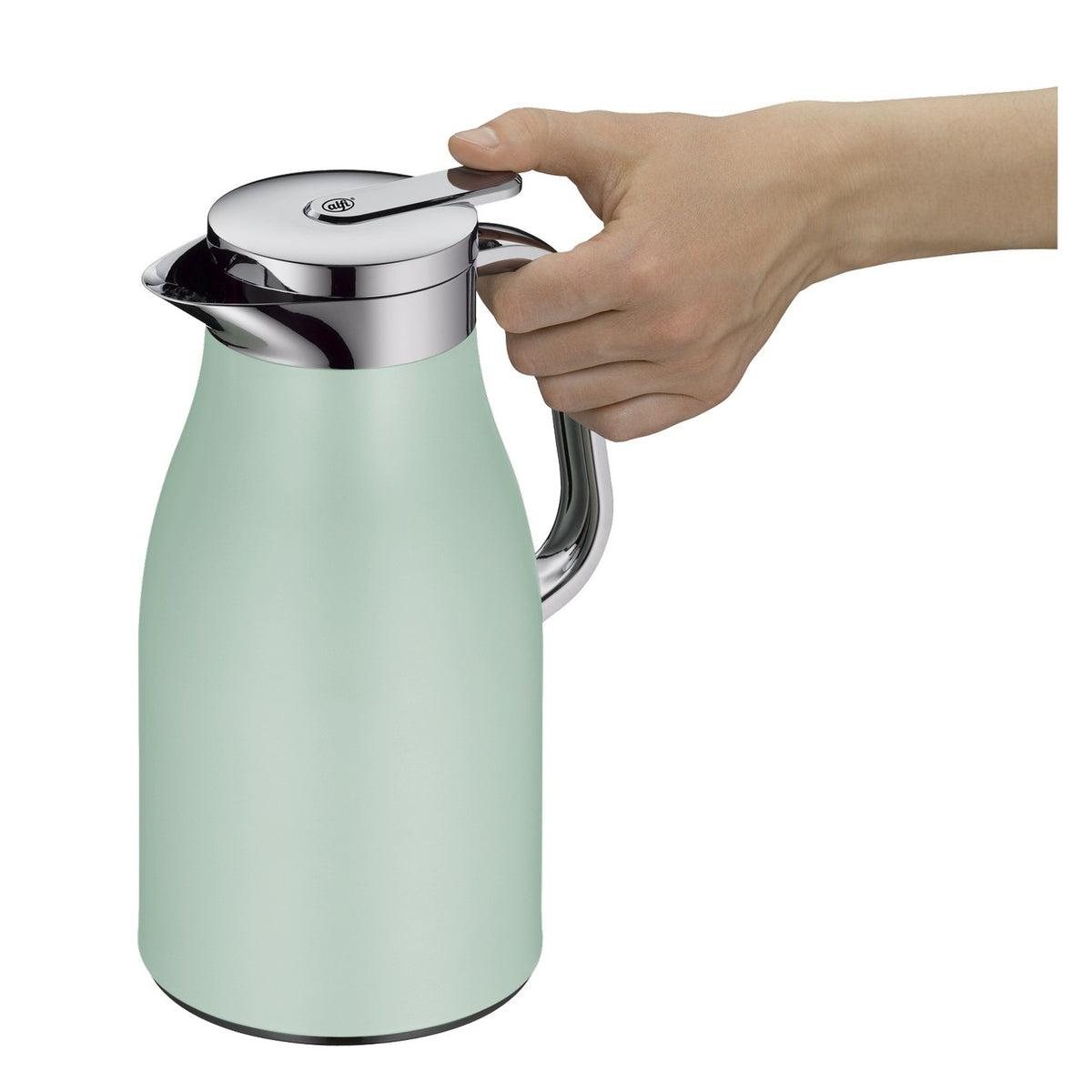 Eine mintgrüne Thermoskanne mit silbernem Deckel steht auf einer Küchentheke. Daneben liegt ein Teller mit Croissants, und ein grünes Küchentuch hängt über der Kante. Im Hintergrund sind ein Fenster mit Bäumen und ein Regal mit Geschirr zu sehen.