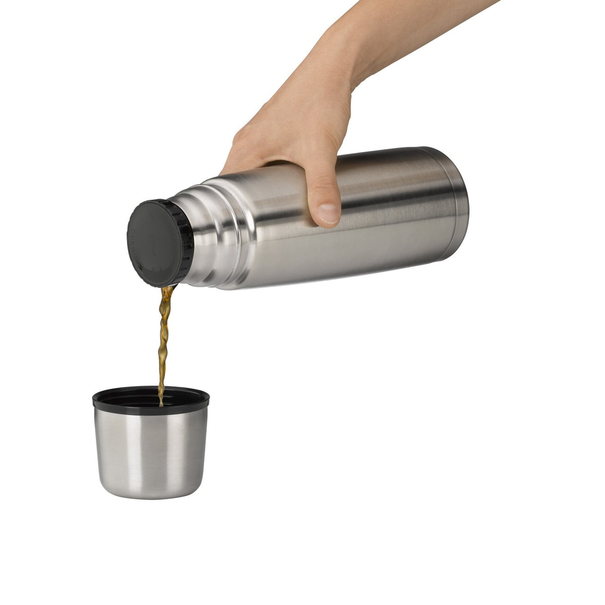 Eine Hand hält eine Edelstahl-Thermoskanne und gießt eine Flüssigkeit in einen passenden Becher darunter. Der Hintergrund ist neutral und hebt die silbernen Objekte hervor.