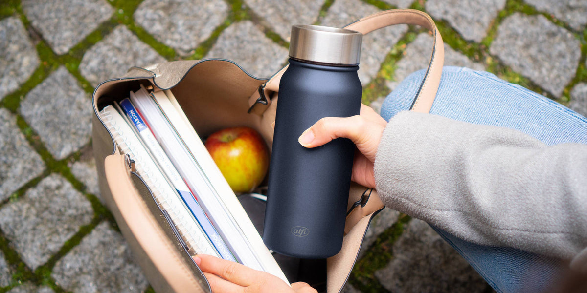 pure drinking mug in hand with books and apple in bag